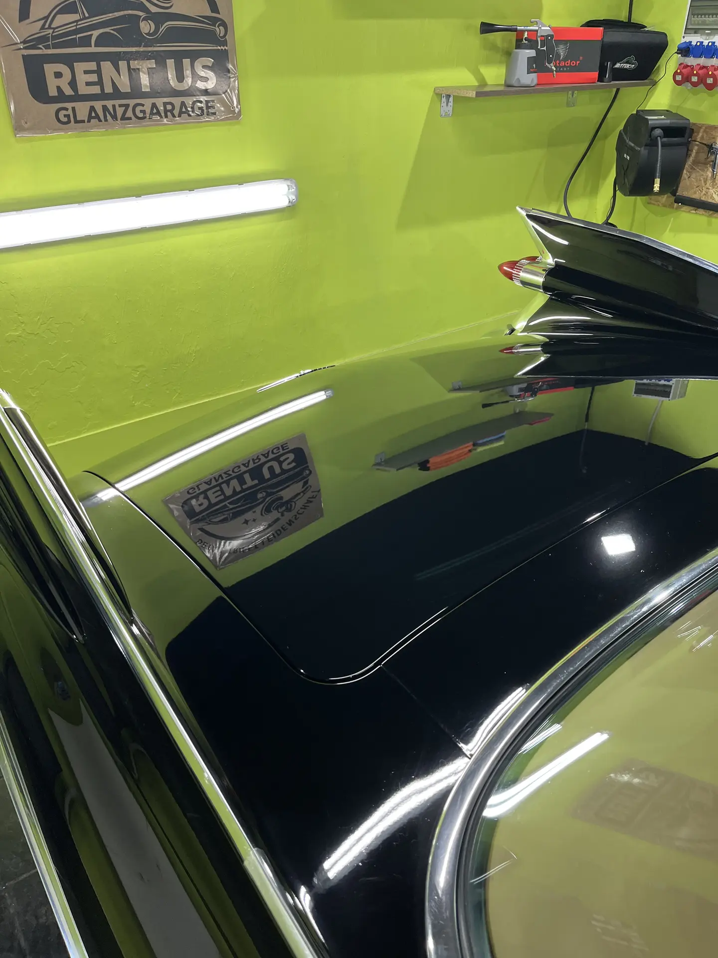 Frisch polierte Heckflosse eines Oldtimers in der Glanzgarage – das RENT-US-Schild spiegelt sich im Lack